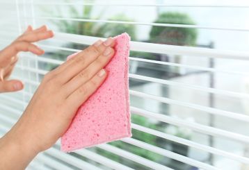 Person cleaning wooden blinds with a microfiber cloth.
